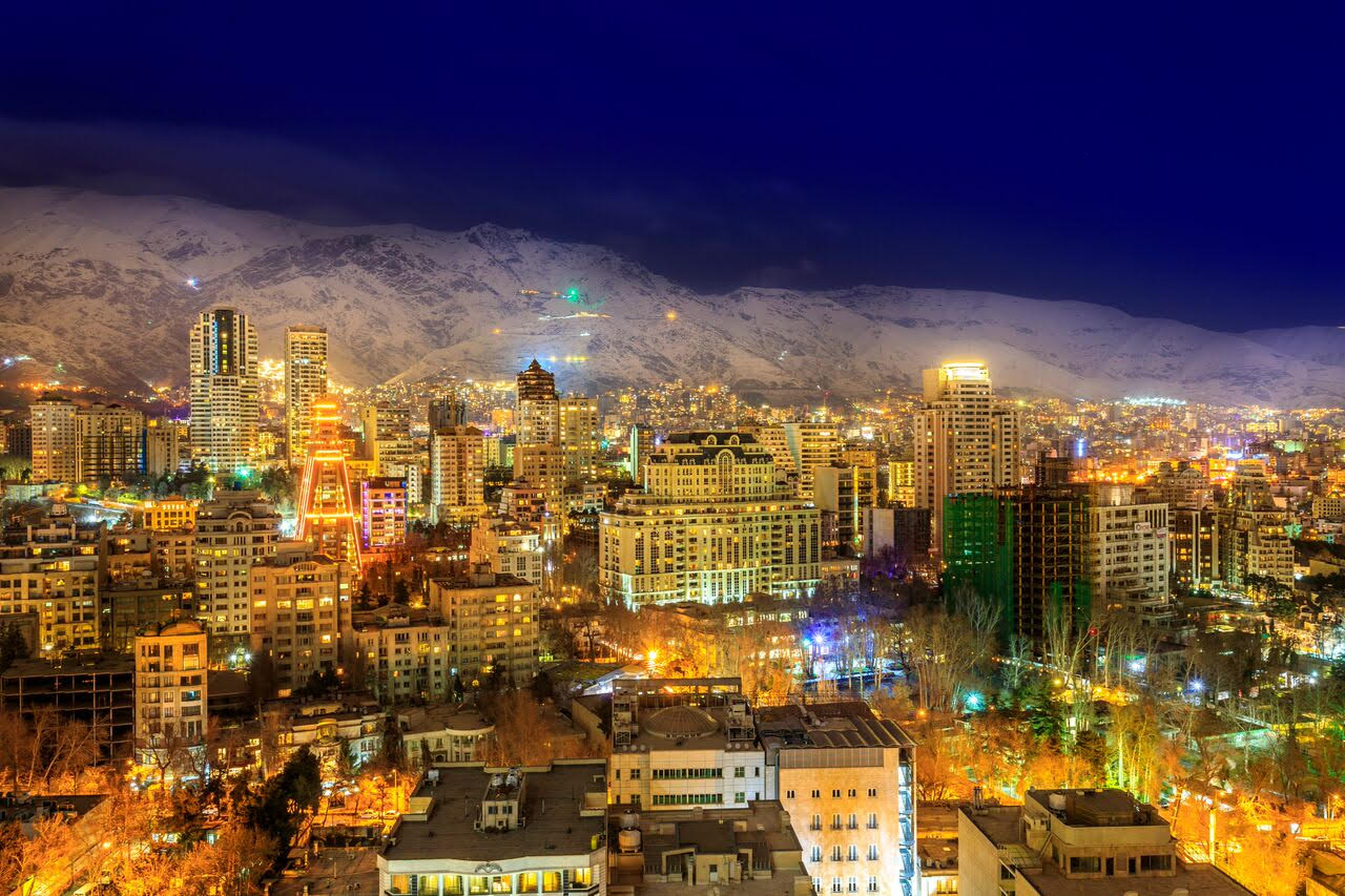 Nighttime cityscape of Tehran with illuminated buildings and the Alborz Mountains in the distance