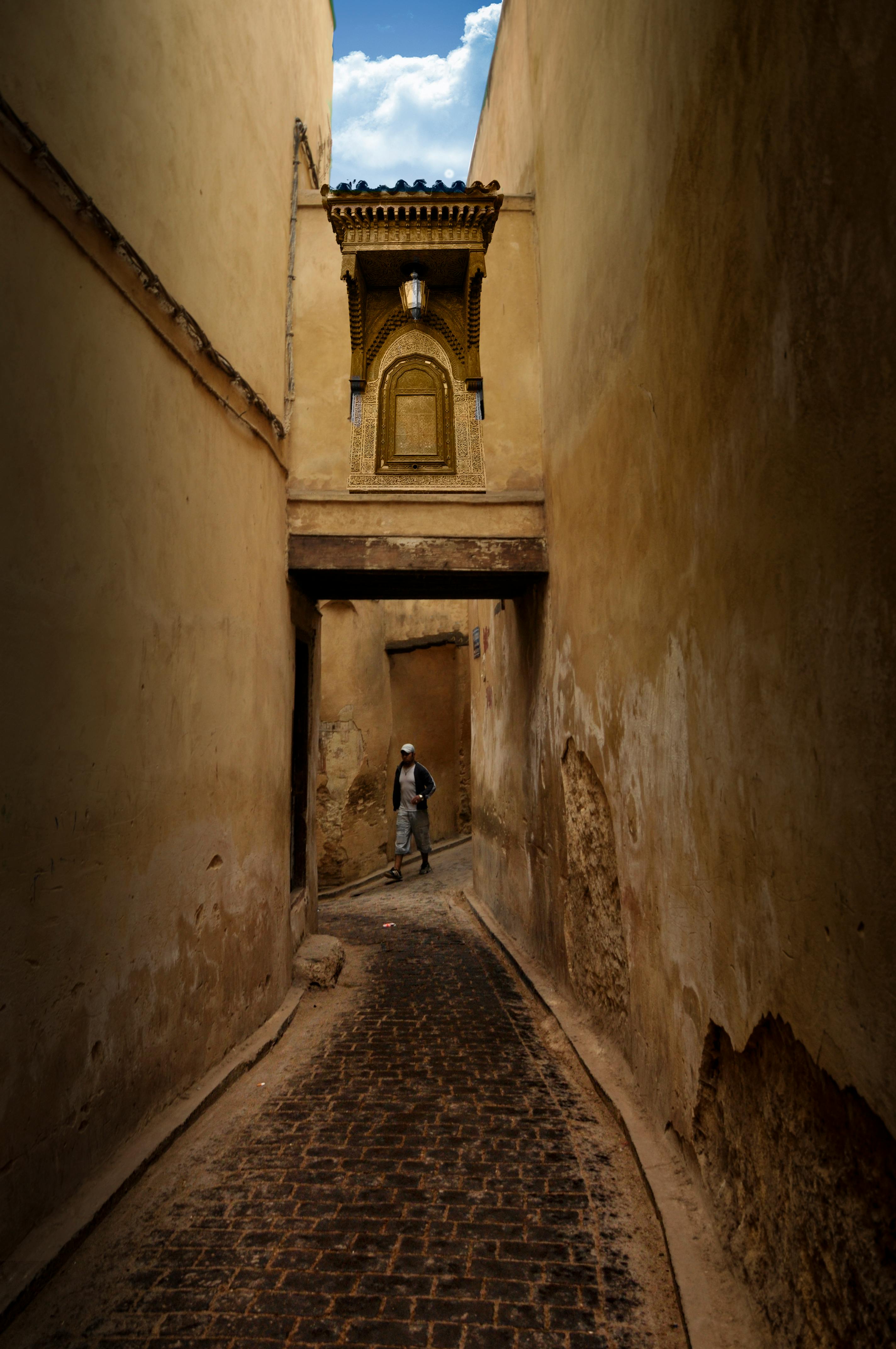 A lone figure walks through the narrow ochre alleyways of Fes el-Bali